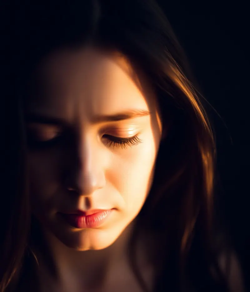 A woman looking down in quiet contemplation, warm light on half her face